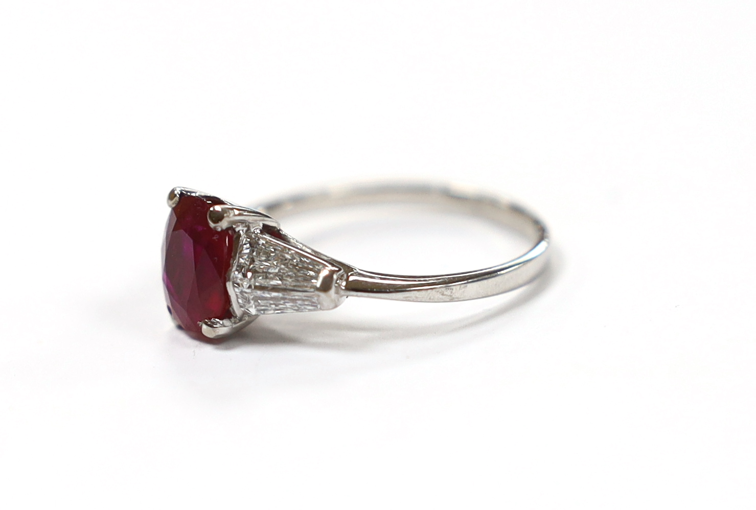 A white metal ruby ring with diamond set shoulders, housed in a Chow Tai Fook box gross weight 3.1grams